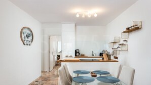 A modern kitchen with white cabinets, a wooden countertop, and a coffee machine. There is a dining area with a glass table and chairs, and a kitchen island with a sink and utensils. - Casa Orquidea 4 (Adeje Miraverde)
