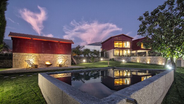 Una casa moderna con piscina, muros de piedra y un edificio rojo al fondo.