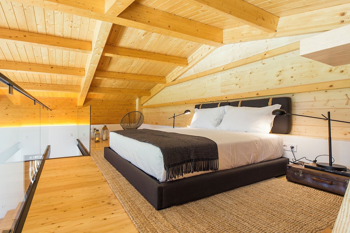 A modern bedroom with a wooden ceiling, a large bed, a chair, and a nightstand.