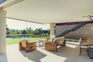 Een ruim terras buiten met houten meubels en uitzicht op een aangelegde tuin en bergen.