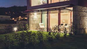 Una casa moderna de dos pisos con fachada de vidrio, zona de estar al aire libre y césped bien cuidado.