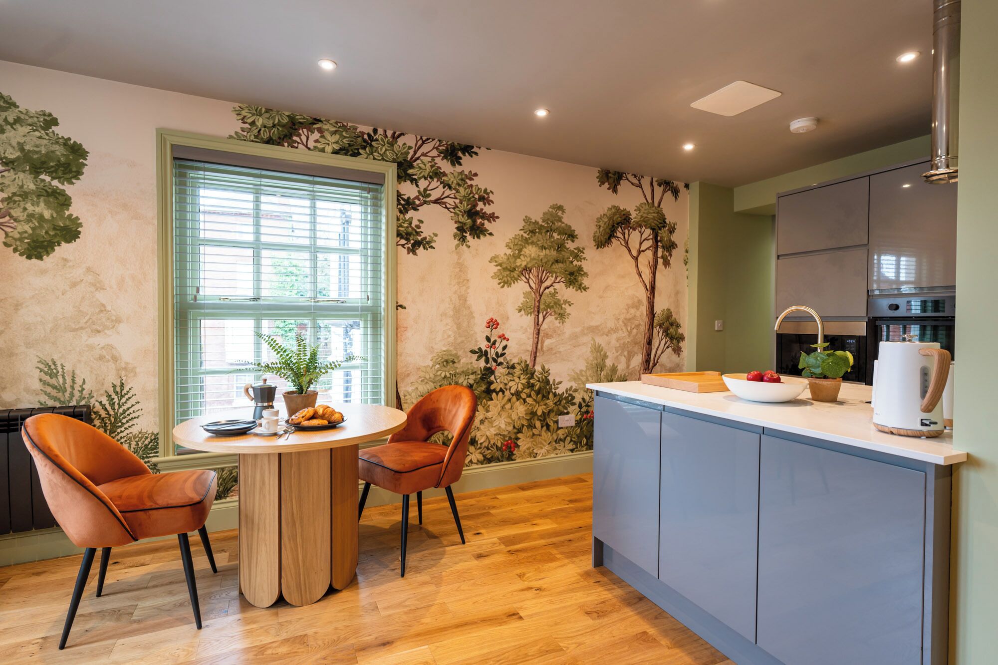 Una cocina moderna con una isla central, suelo de madera y un ventanal con persianas.