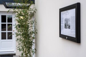 A framed informational plaque mounted on a wall, with a window and a plant visible in the background.