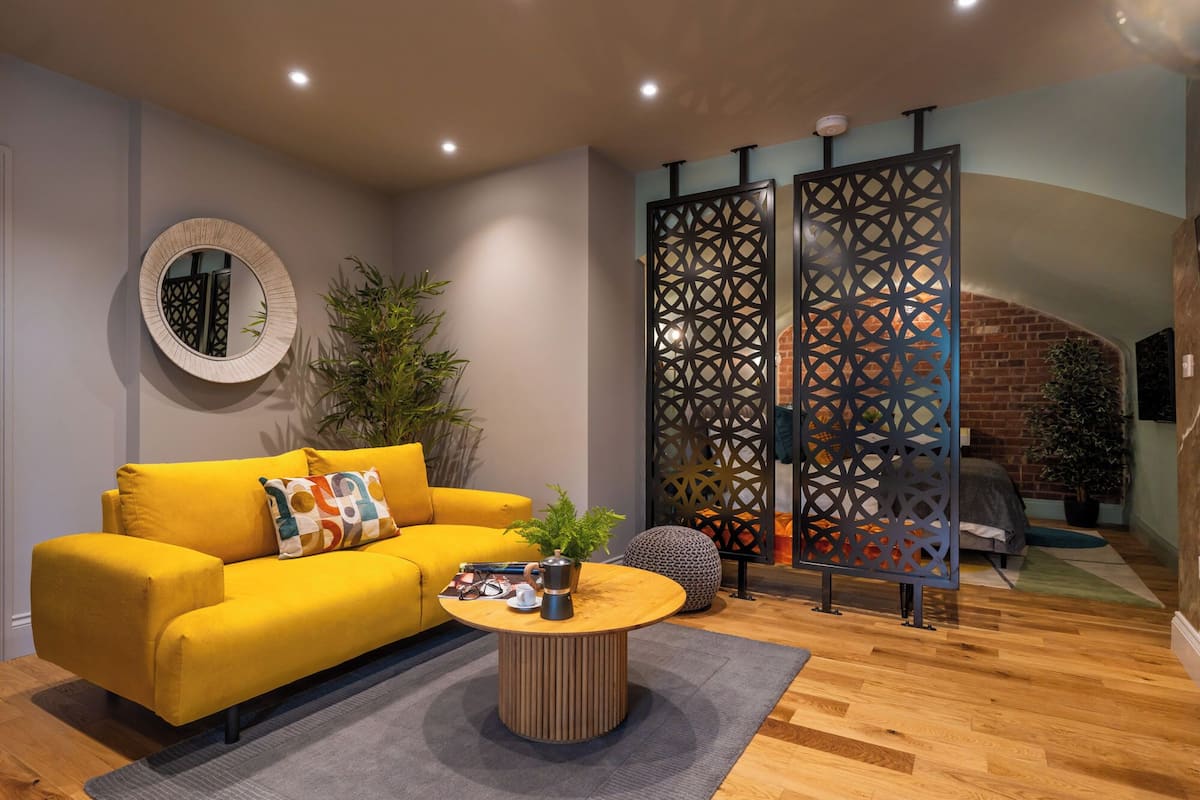 Un salon moderne avec un canapé jaune, une table basse ronde et un paravent décoratif.