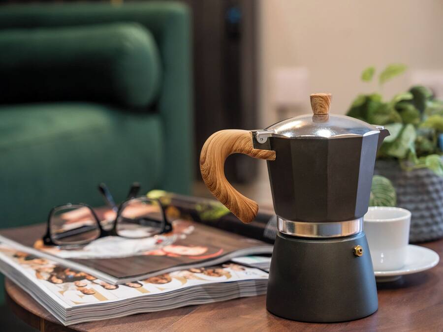 Eine Kaffeemaschine auf einem Tisch, zusammen mit einer Zeitschrift, Gläsern und einer Tasse.