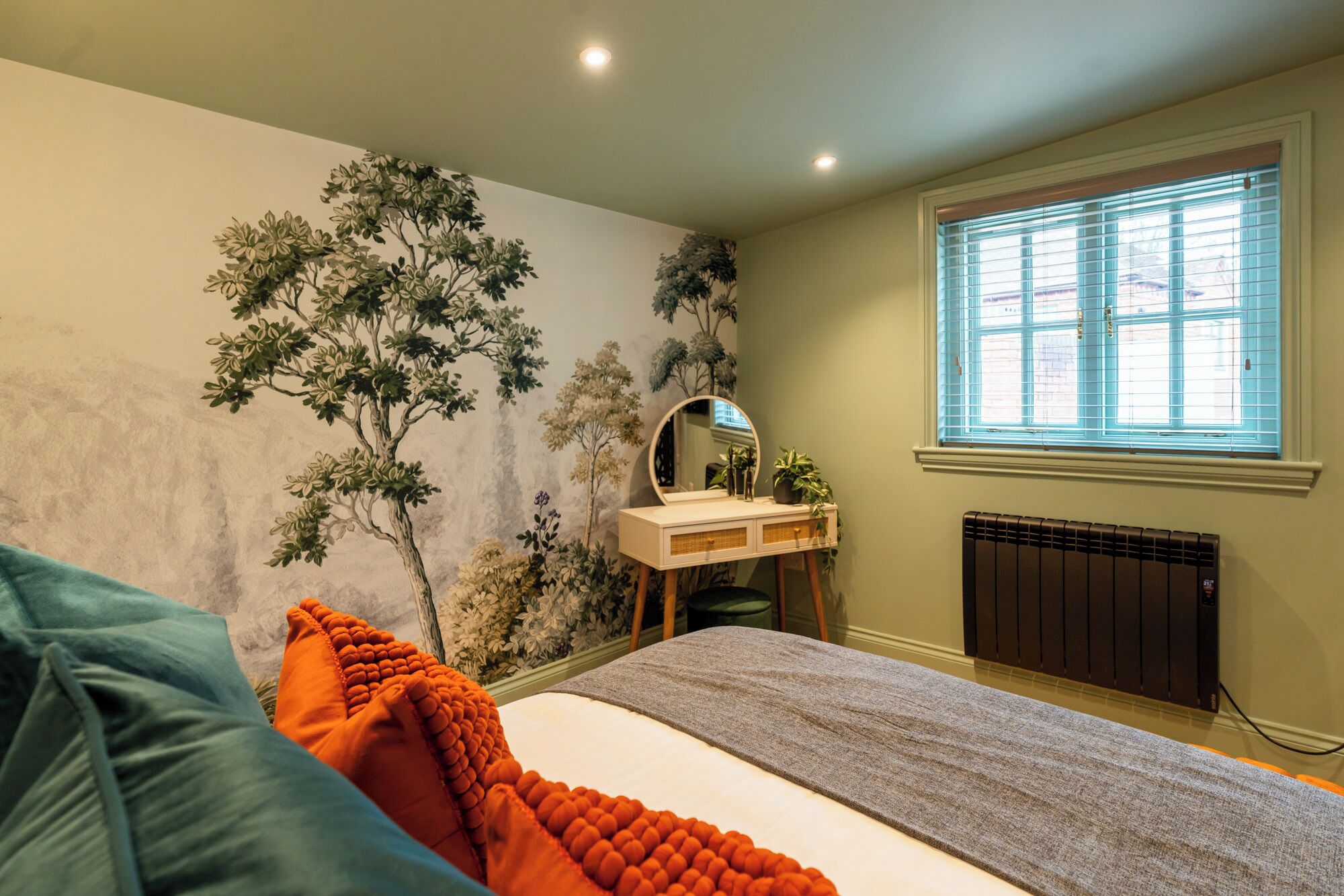Une chambre à coucher avec un lit, une commode avec un miroir, un radiateur et une fenêtre avec des stores.