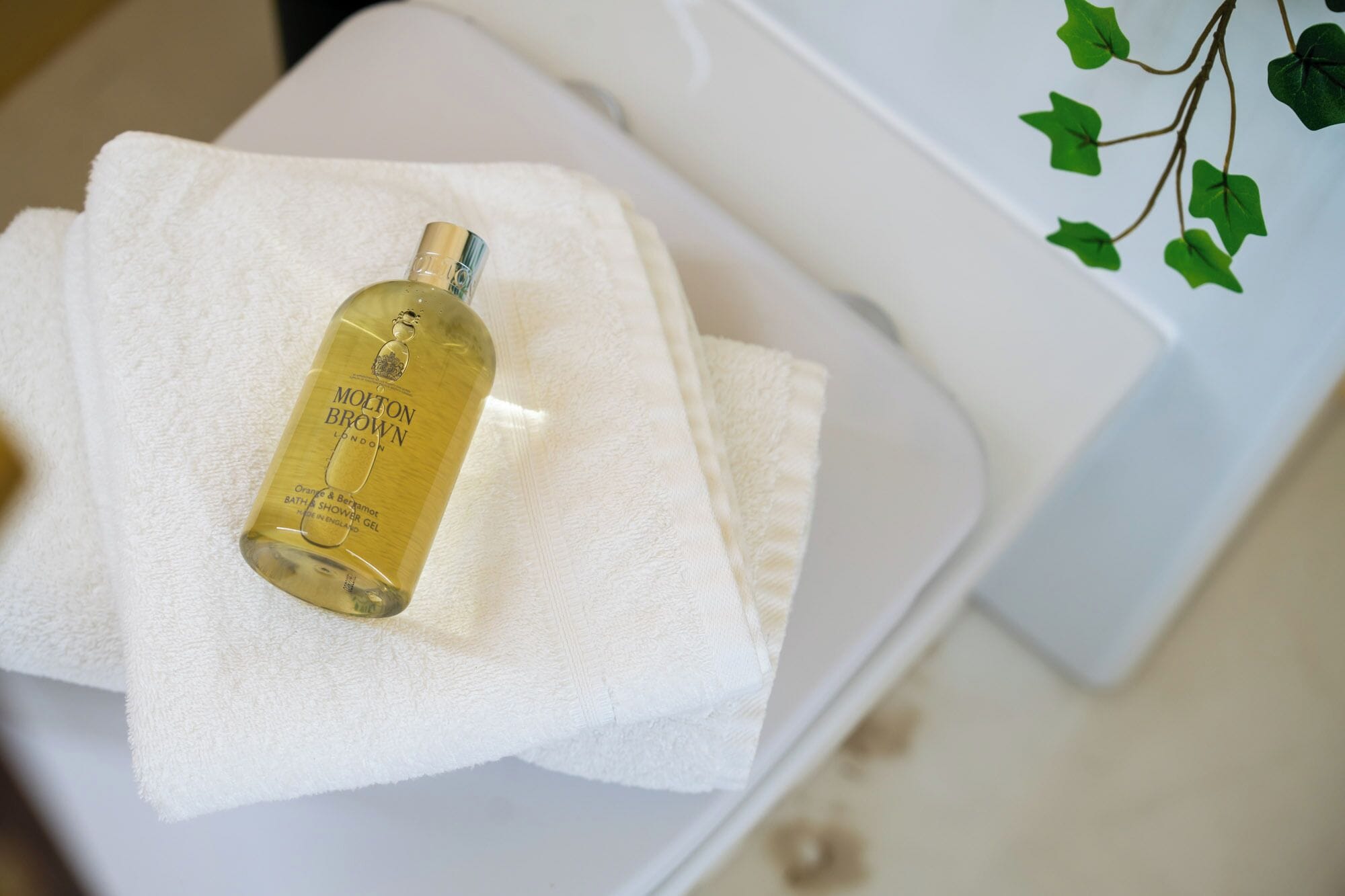 A bottle of Molton Brown shower gel on a white towel in a bathroom.