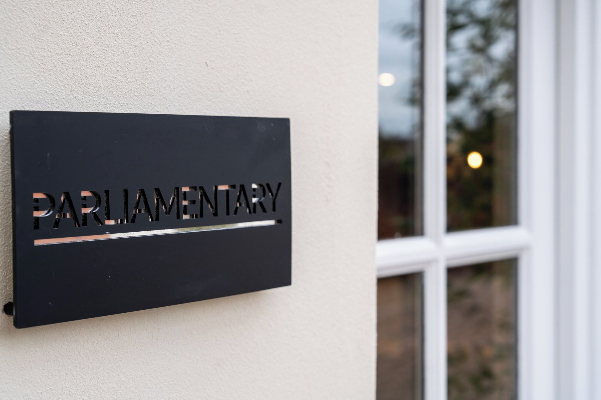 A black sign with the word "PARLIAMENTARY" on a wall next to a window.