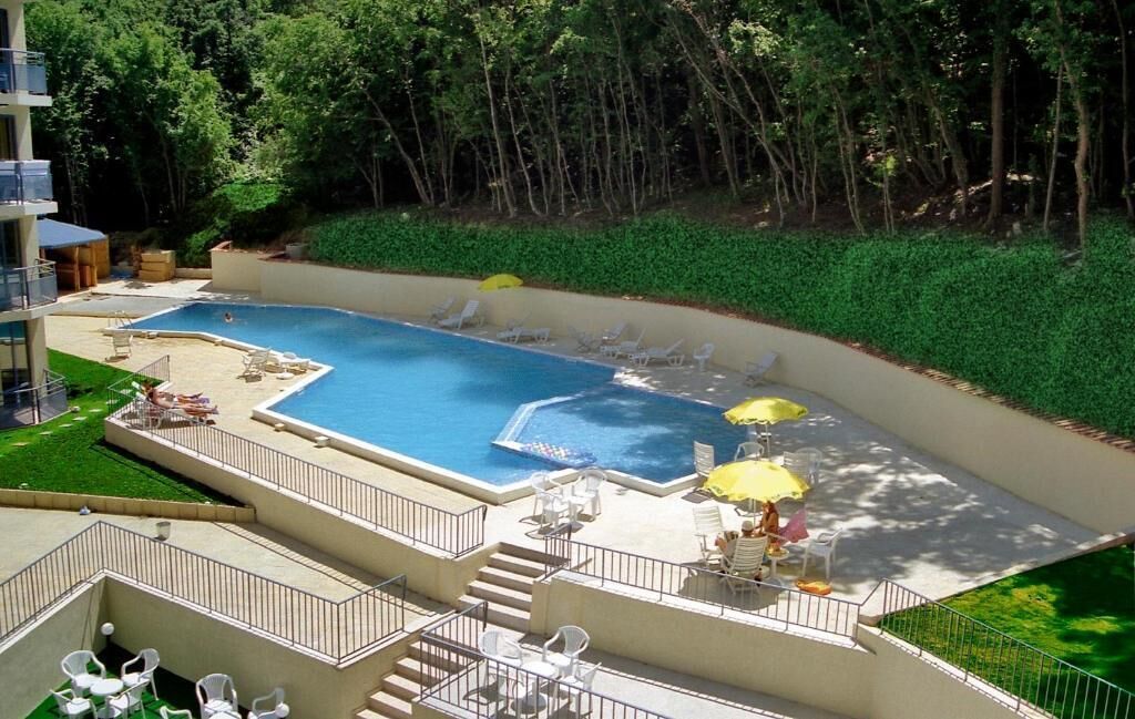 Un área de piscina con varias secciones, sillas de descanso y sombrillas.