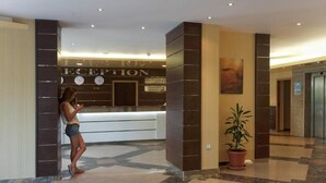 A reception area with a reception desk, a clock, and a potted plant. - Regina Hotel (Varna)