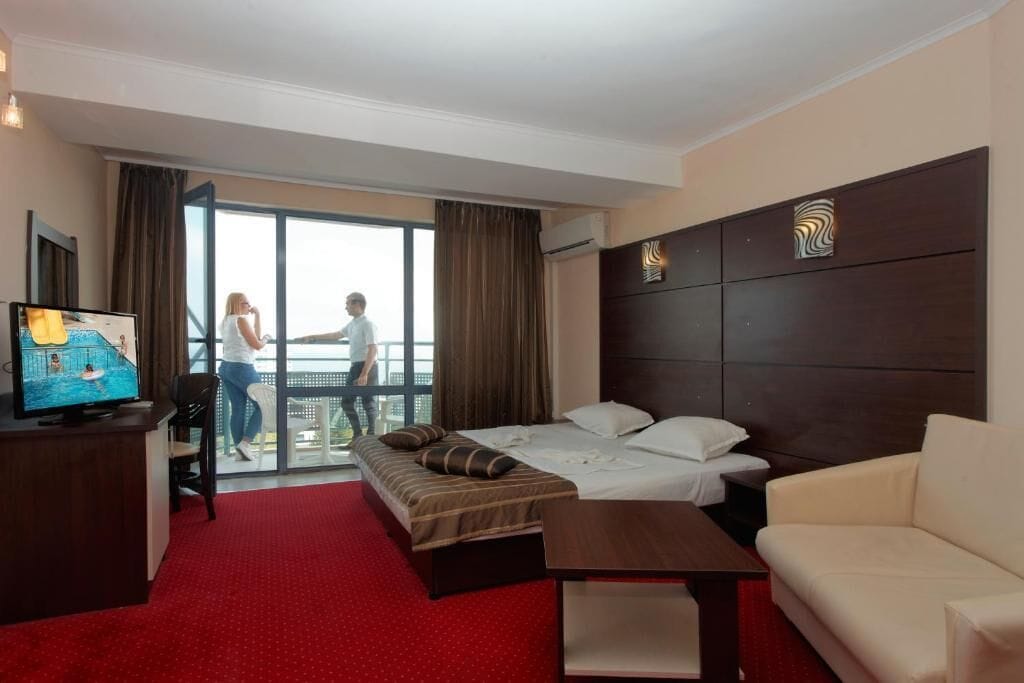 A hotel room with a bed, a sofa, a TV, and a balcony with a view.