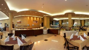 A spacious buffet area with multiple round tables, a central serving station, and a high ceiling with recessed lighting. - Regina Hotel (Varna)
