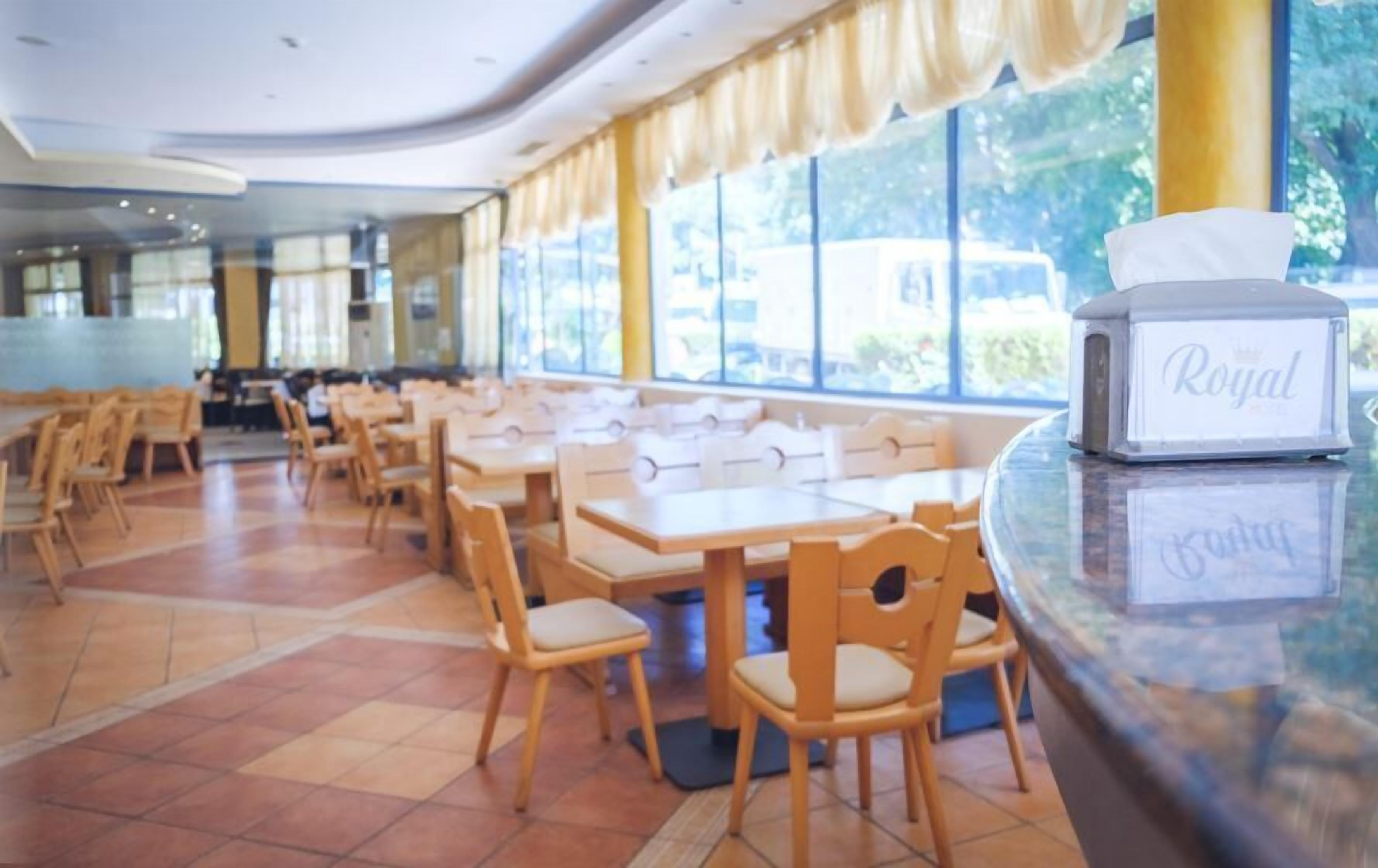 Un vaste espace dédié à la salle à manger, avec des tables et des chaises en bois, de grandes fenêtres et un comptoir muni d’un distributeur de mouchoirs.