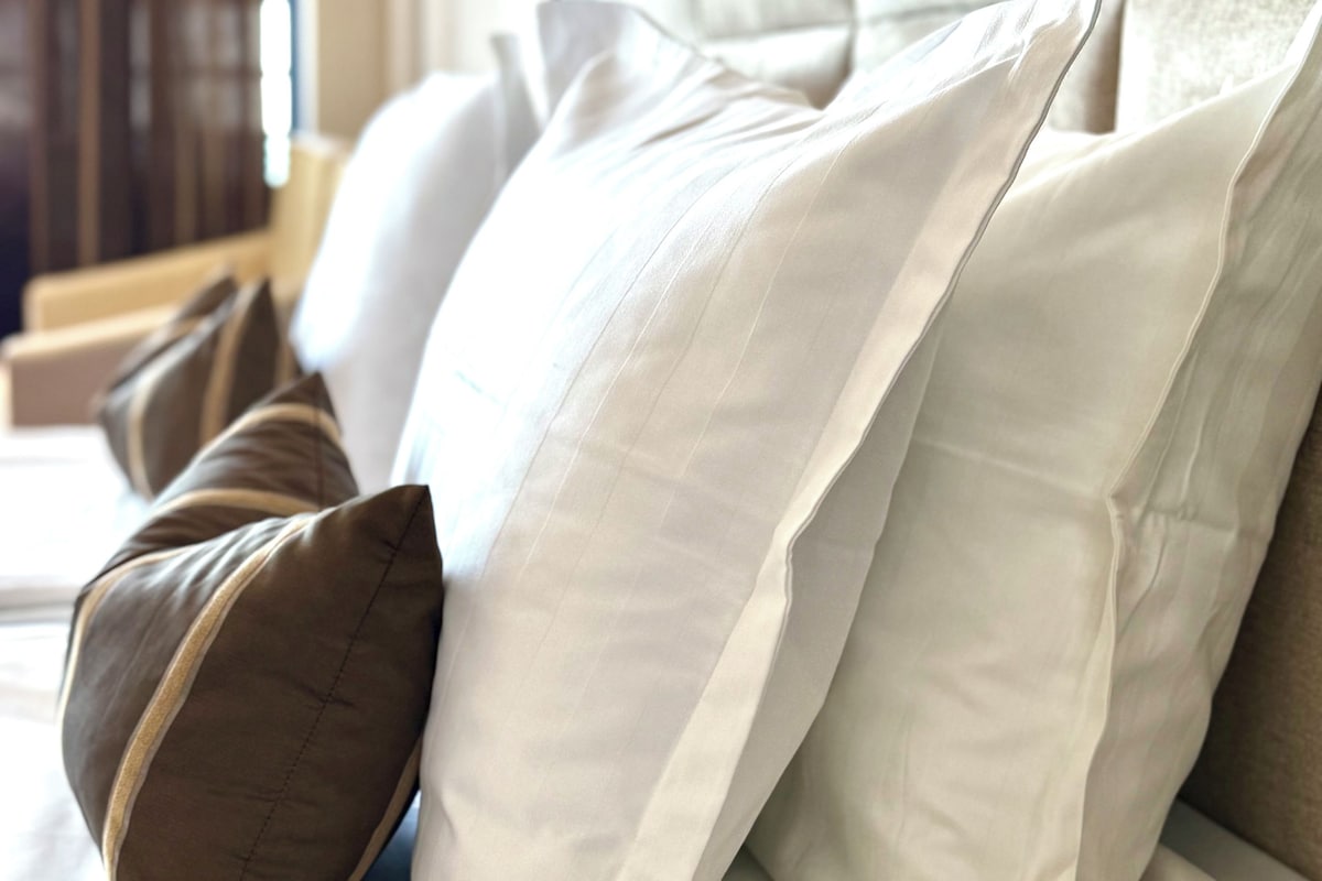 A bed with multiple pillows, a headboard, and a window with curtains.