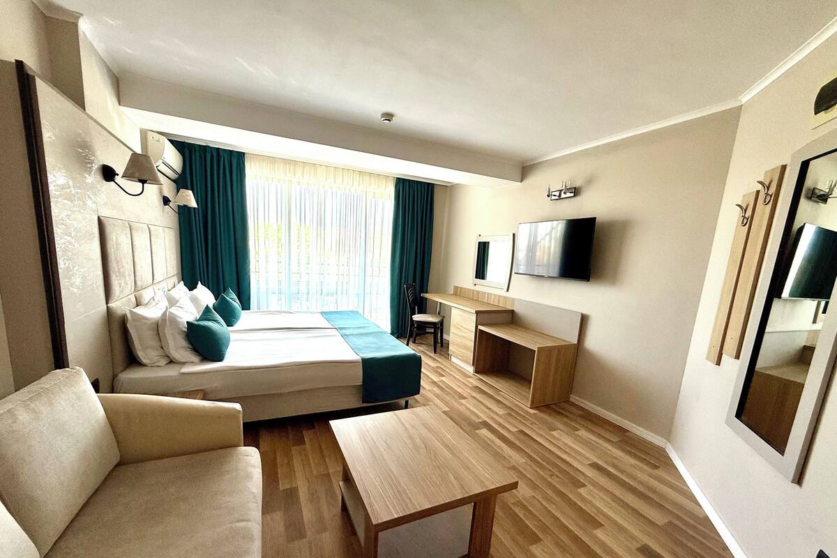 A modern hotel room with a bed, sofa, desk, and TV.