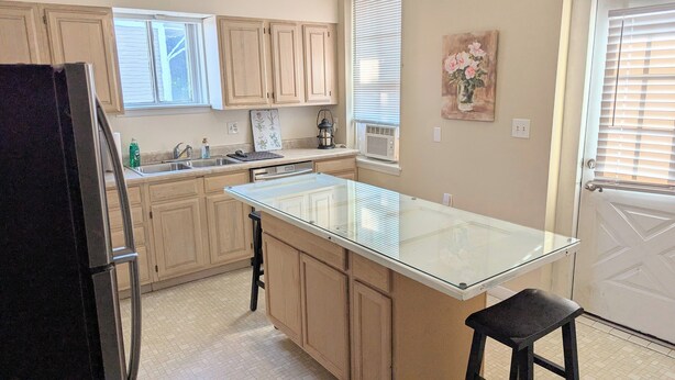 A kitchen with wooden cabinets, a refrigerator, a sink, and a glass-top island with a stool. - Relaxing Rustic Oasis II -  6 min walk to Downtown! Cyclist Welcomed! (Cumberland)