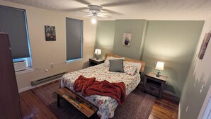 A bedroom with a bed, two bedside tables, a heater, a ceiling fan, and two windows with blinds. - Relaxing Rustic Oasis II -  6 min walk to Downtown! Cyclist Welcomed! (Cumberland)