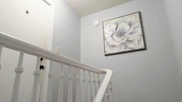 A staircase with white balusters and a white handrail, leading to a room with a light gray wall and a framed floral artwork.