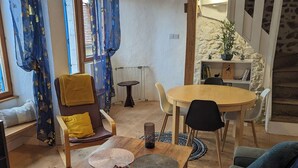 Una sala acogedora con una mesa de madera, un sofá y una silla. Hay una mesita con una lámpara y una estantería con libros y una planta.