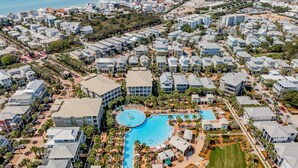 An aerial view of a resort with a central pool, multiple buildings, and a surrounding landscape.