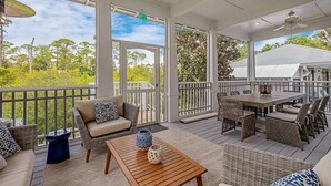 A covered outdoor area with wicker furniture, a wooden table, and a view of the surrounding greenery.