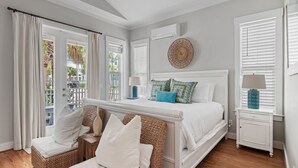 A bedroom with a bed, two bedside tables, a wicker chair, and a view of the outside.