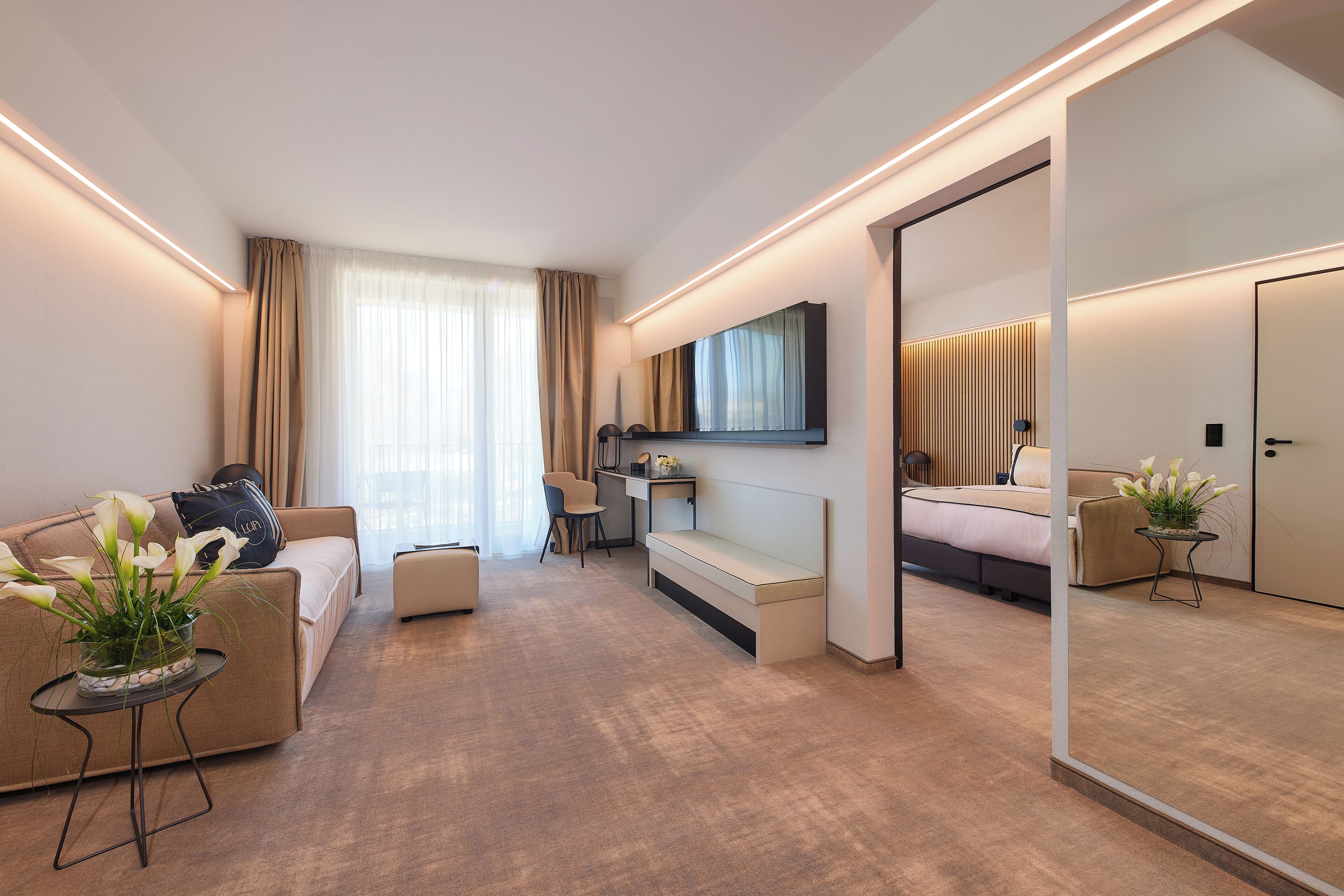 A modern hotel room with a sofa, a desk, a bed, and a large mirror.