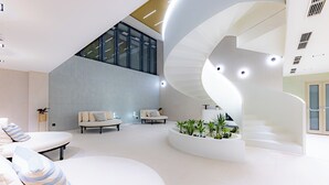 A spacious, modern interior with a curved staircase, a seating area with sofas, and a plant arrangement. - LUA Resort Balatonfüred (Balatonfured)