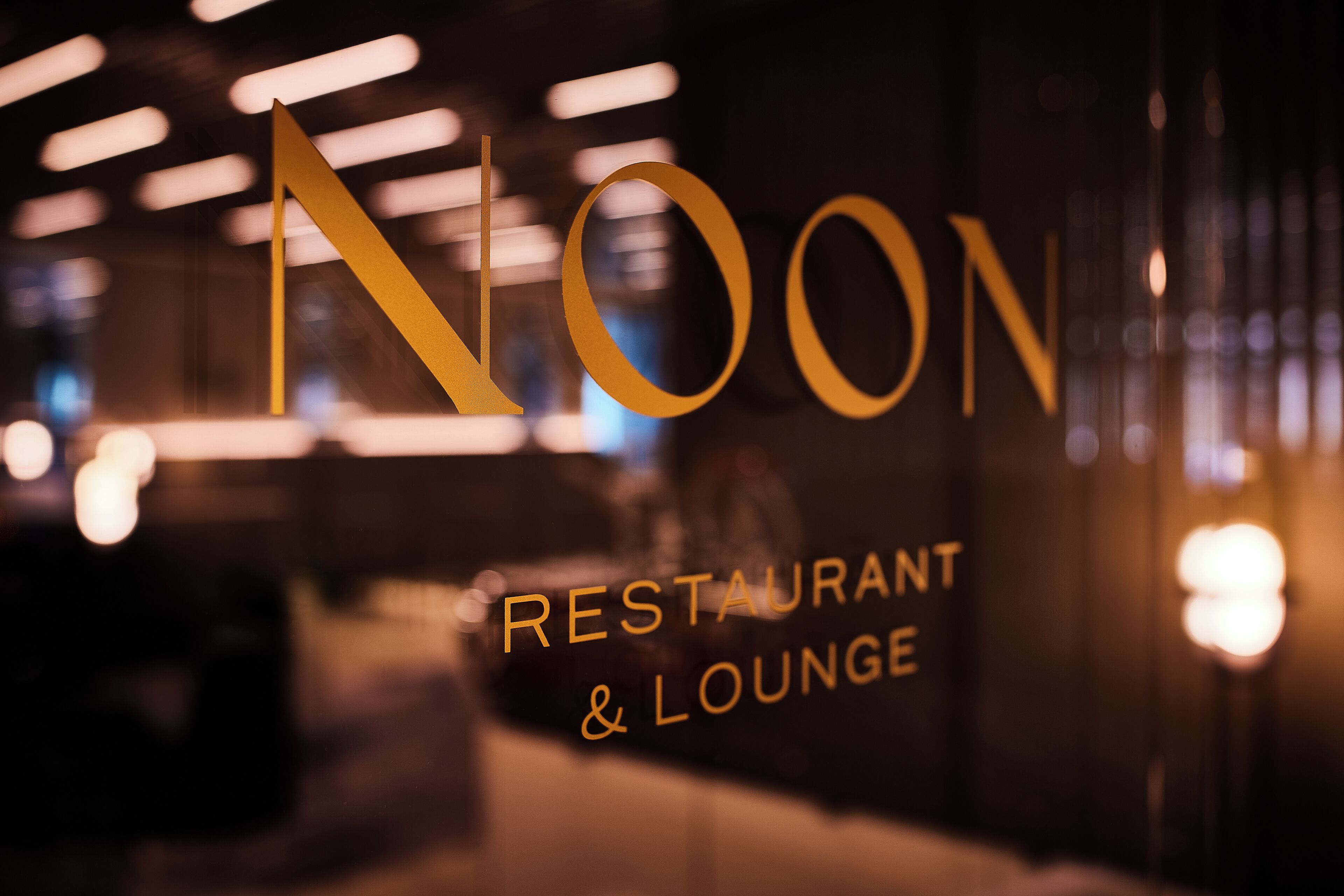 A blurred interior view of a restaurant and lounge with the word "NOON" prominently displayed.