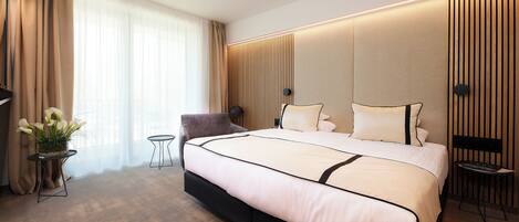 Una habitación de hotel moderna con una cama grande, una mesita con una planta, una silla y un escritorio con una lámpara.