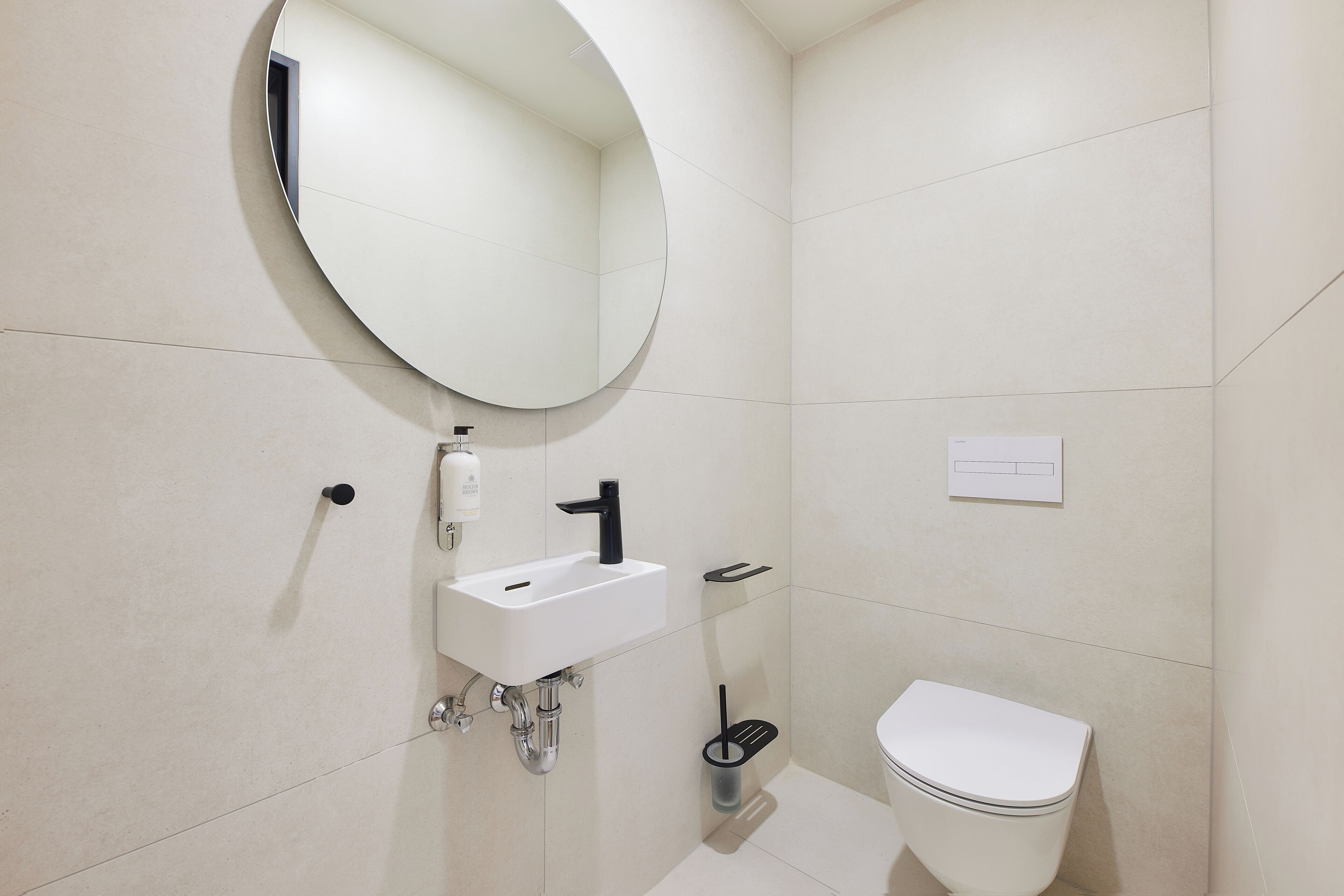 Un baño moderno con un espejo redondo, un lavamanos blanco y un inodoro.