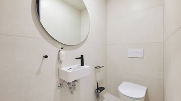 Un baño moderno con un espejo redondo, un lavamanos blanco y un inodoro.
