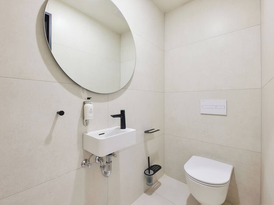 Un baño moderno con un espejo redondo, un lavamanos blanco y un inodoro.