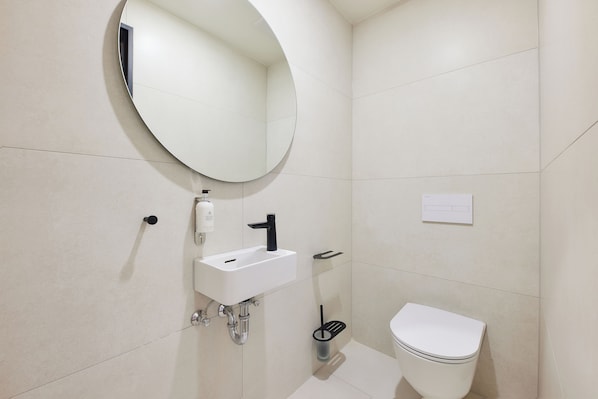 Une salle de bain moderne avec un miroir rond, un lavabo blanc et des toilettes.