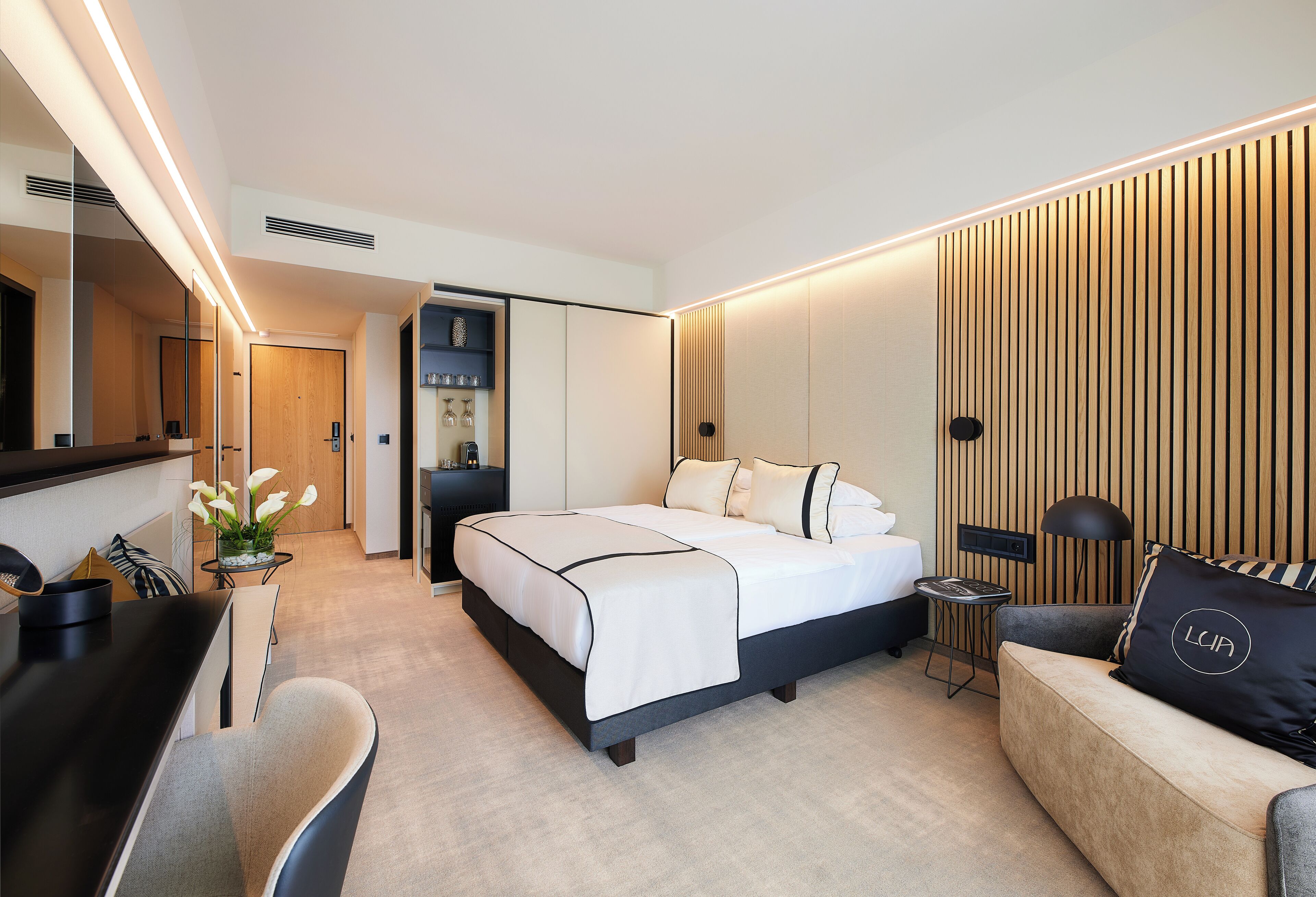 Quarto de hotel moderno com uma cama grande, uma escrivaninha, um sofá e um espelho.