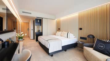 A modern hotel room with a large bed, a desk, a sofa, and a mirror.