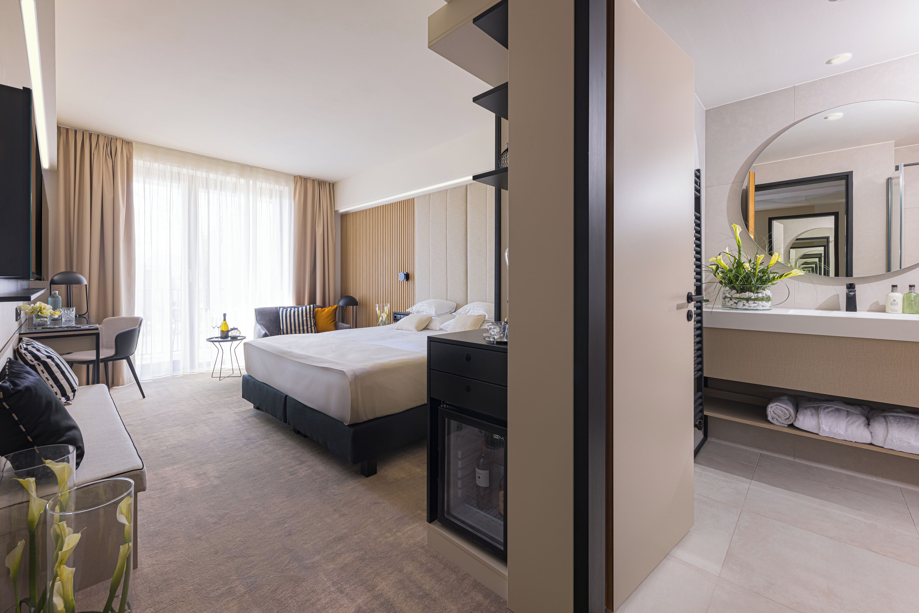Ein modernes Hotelzimmer mit Bett, Nachttisch, Schreibtisch, Stuhl und einem großen Spiegel.