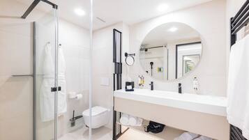 A modern bathroom with a glass shower enclosure, a white sink with a round mirror, and neatly arranged toiletries.