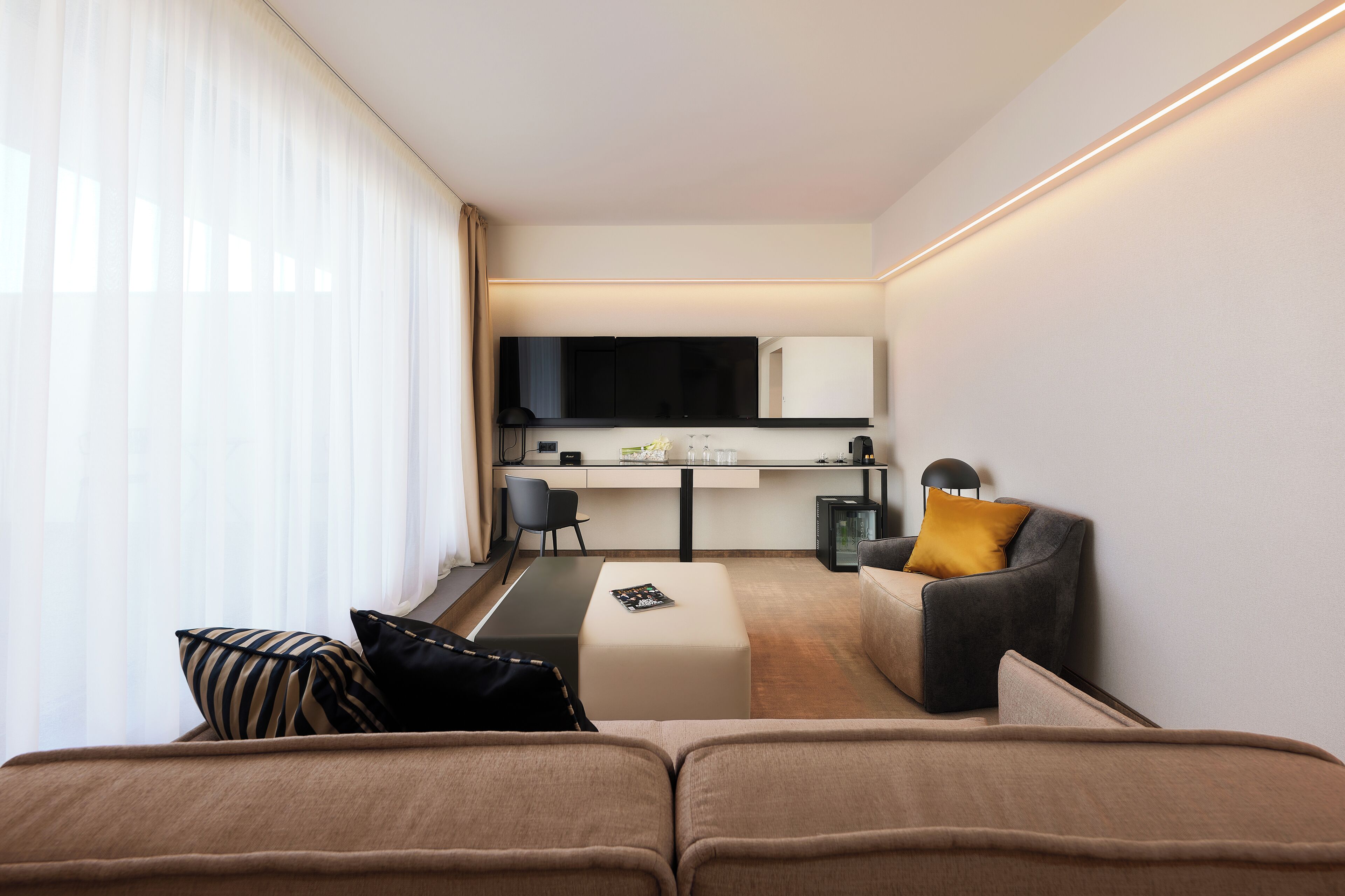 A modern hotel room with a sofa, a small desk, a chair, and a television.