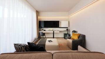 A modern hotel room with a sofa, a small desk, a chair, and a television.