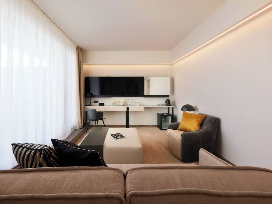 A modern hotel room with a sofa, a small desk, a chair, and a television.