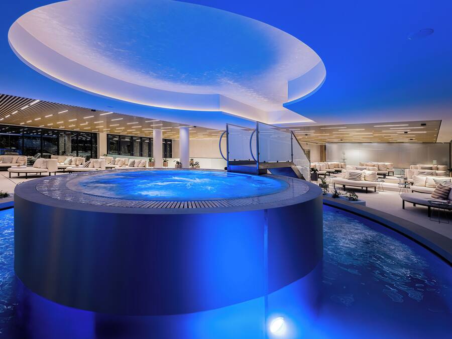 Un área de piscina interior moderna con un jacuzzi circular, asientos tipo lounge y un diseño de techo singular.