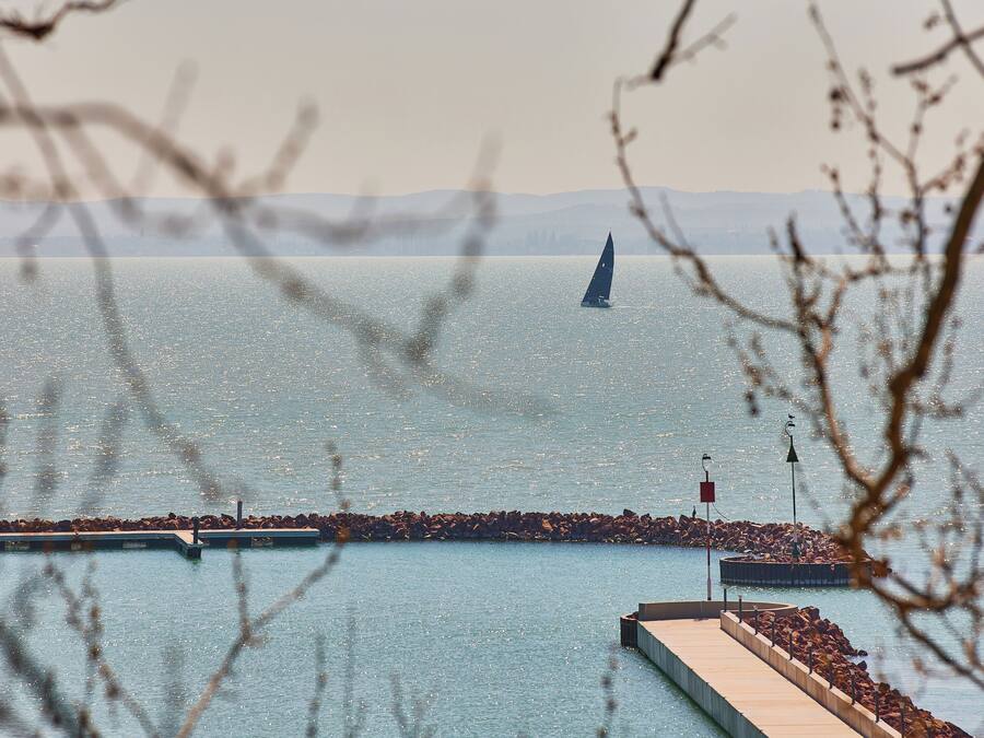 A pier extending into calm water with a sailboat in the distance and mountains in the background.