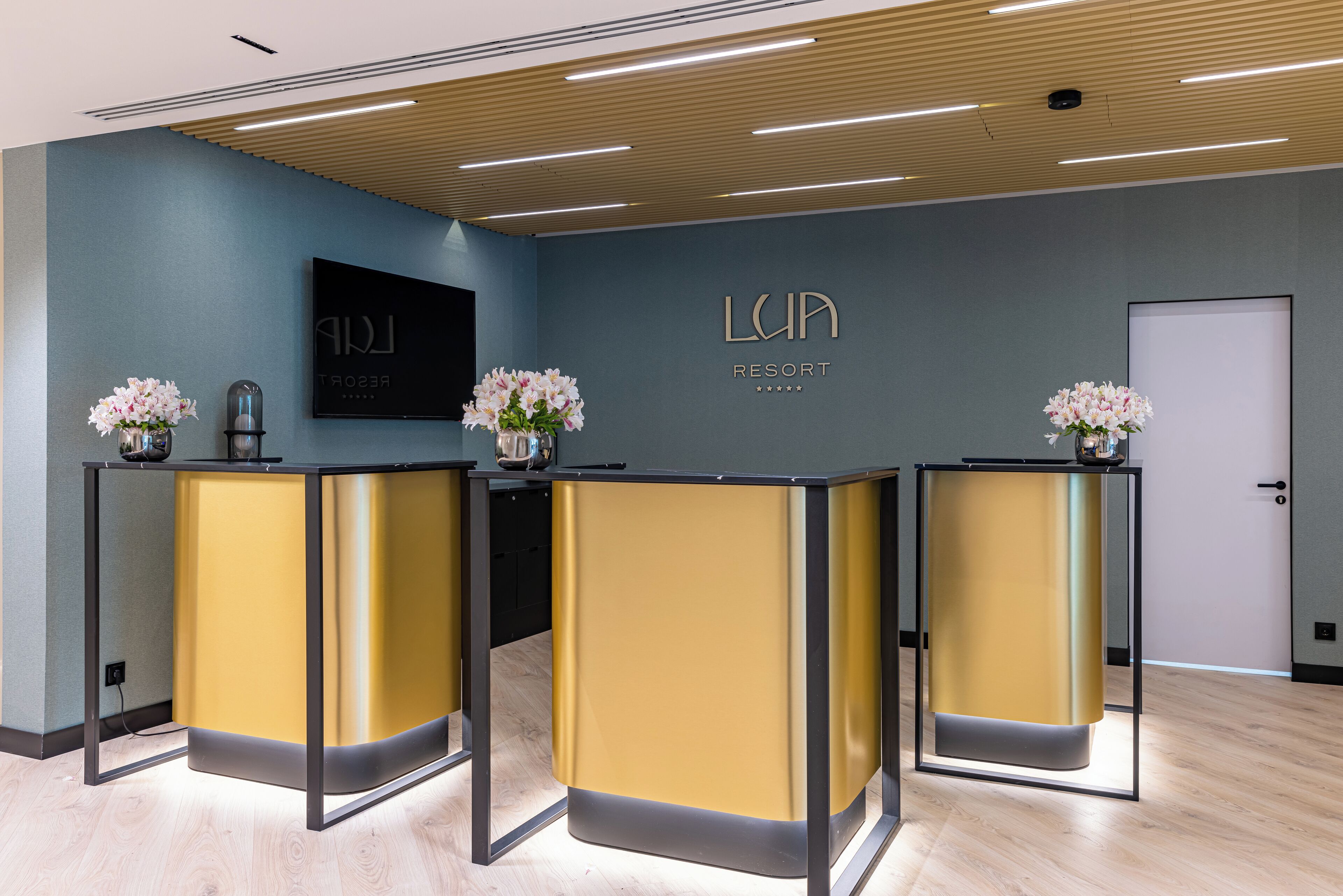 Un espace d’accueil comprenant trois comptoirs de réception, un téléviseur fixé au mur et une enseigne murale indiquant « LUPA RESORT ».