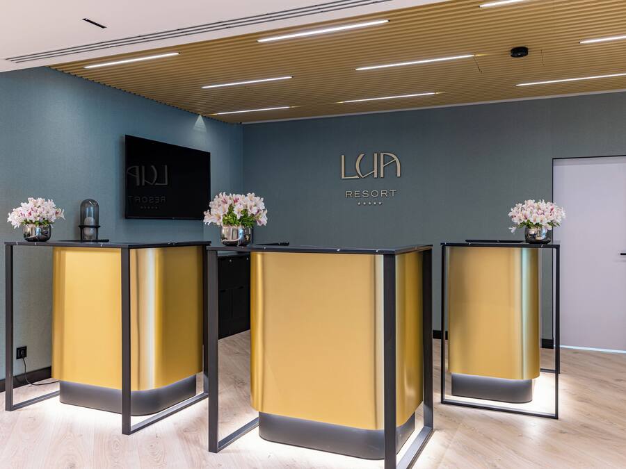 Un espace d’accueil comprenant trois comptoirs de réception, un téléviseur fixé au mur et une enseigne murale indiquant « LUPA RESORT ».
