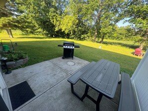 Une terrasse avec un barbecue, une table et un petit coin jardin.