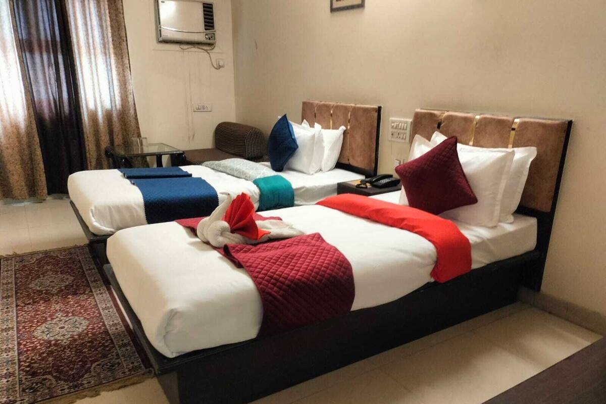 A hotel room with two beds, each with a headboard, a bedside table, and a red and white blanket.