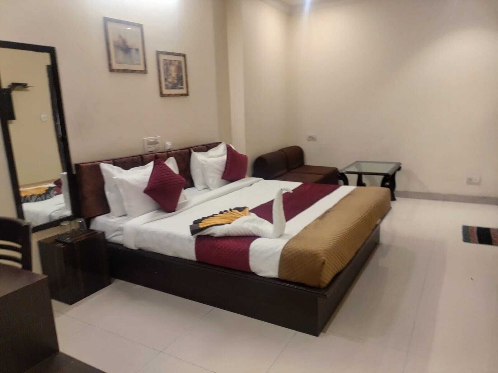 A hotel room with a large bed, a desk, and a chair. There are two framed pictures on the wall.