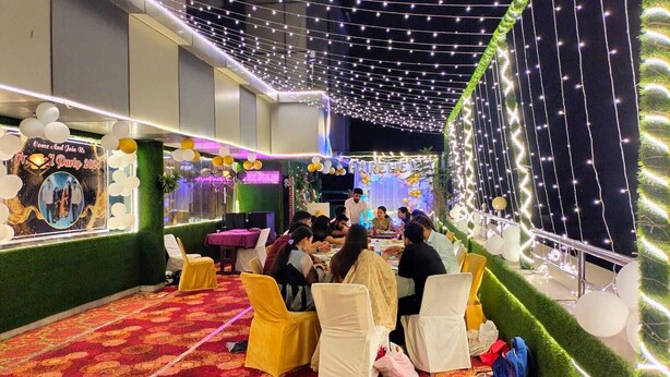 A decorated indoor event space with tables and chairs, string lights, and a stage area. - Hotel Jagat inn (Haridwar)
