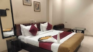 A neatly made bed with a brown blanket, white and red pillows, and a decorative swan pillow. There is a small table with a glass top next to the bed. - Hotel Jagat inn (Haridwar)